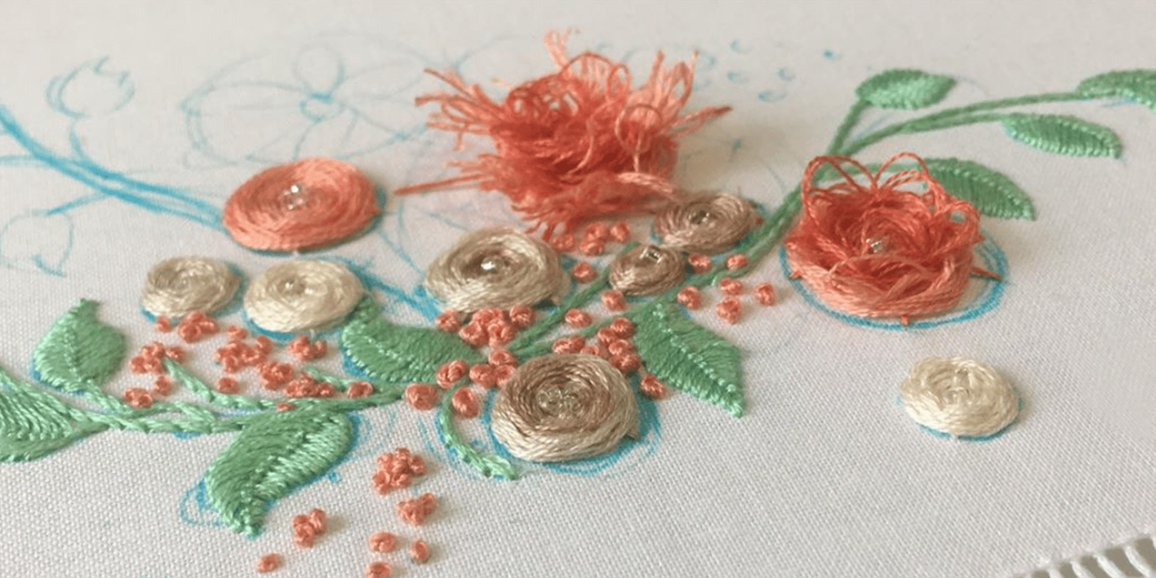 A photo of  salmon-colored flowers being embroidered onto white fabric.